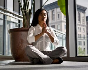 Femme dans un bureau vitré en position du lotus, mains jointes.